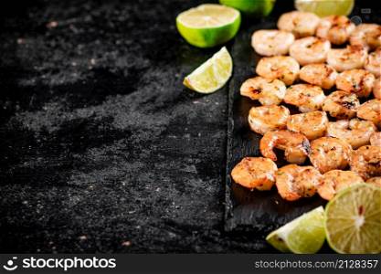 Grilled shrimp on a stone board with pieces of lime. On a black background. High quality photo. Grilled shrimp on a stone board with pieces of lime.