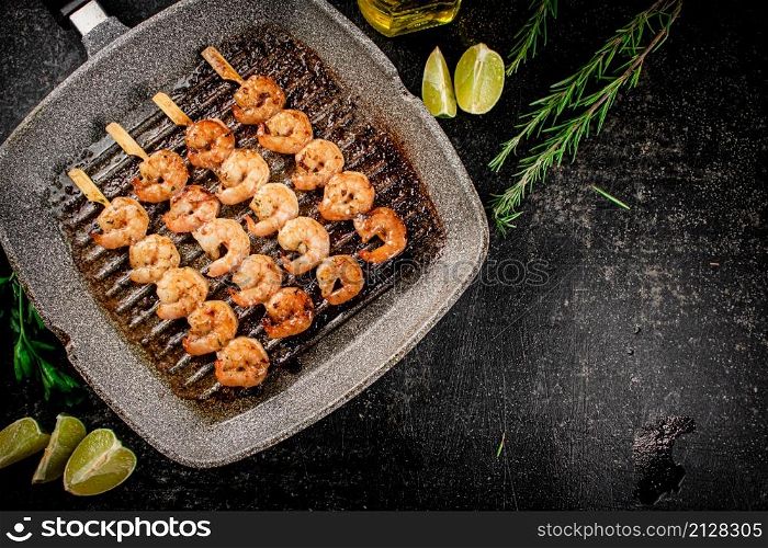 Grilled shrimp on skewers in a frying pan with rosemary and pieces of lime. On a black background. High quality photo. Grilled shrimp on skewers in a frying pan with rosemary and pieces of lime.