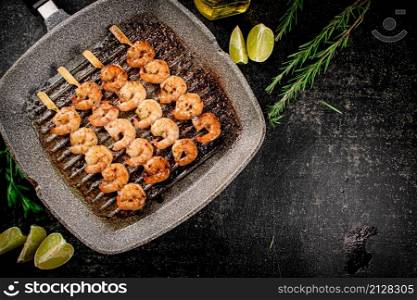 Grilled shrimp on skewers in a frying pan with rosemary and pieces of lime. On a black background. High quality photo. Grilled shrimp on skewers in a frying pan with rosemary and pieces of lime.