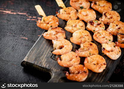 Grilled shrimp on skewers on a cutting board. Against a dark background. High quality photo. Grilled shrimp on skewers on a cutting board.