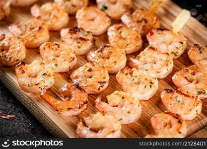 Grilled shrimp on skewers on a cutting board. Against a dark background. High quality photo. Grilled shrimp on skewers on a cutting board.