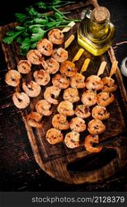Grilled shrimp on skewers with parsley on a cutting board. Against a dark background. High quality photo. Grilled shrimp on skewers with parsley on a cutting board.