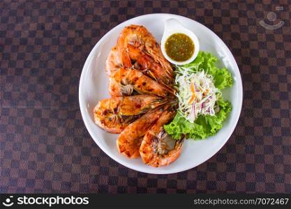 Grilled shrimps with seafood decorated with vegetable and hot spicy dipping sauce in white ceramic dish put on leather floor the grid pattern. Top view