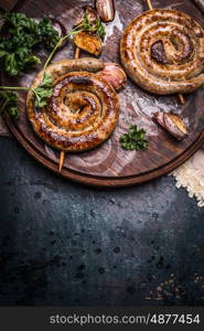 Grilled spiral sausages with garlic and seasoning on dark wooden background, top view, place for text