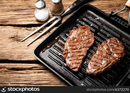 Grilled steak in a frying pan. On a wooden background. High quality photo. Grilled steak in a frying pan.
