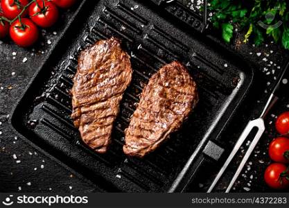 Grilled steak in a frying pan with tomatoes and spices. On a black background. High quality photo. Grilled steak in a frying pan with tomatoes and spices.