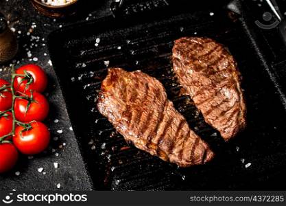 Grilled steak in a frying pan with tomatoes and spices. On a black background. High quality photo. Grilled steak in a frying pan with tomatoes and spices.