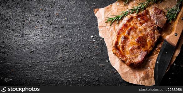 Grilled steak on paper with a knife and a sprig of rosemary. Against a dark background. High quality photo. Grilled steak on paper with a knife and a sprig of rosemary.
