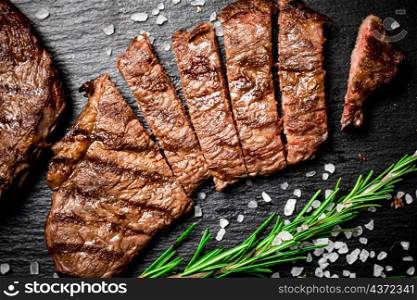 Grilled steak with a sprig of rosemary. On a black background. High quality photo. Grilled steak with a sprig of rosemary.