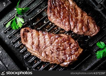 Grilled steak with parsley in a frying pan. On a black background. High quality photo. Grilled steak with parsley in a frying pan.