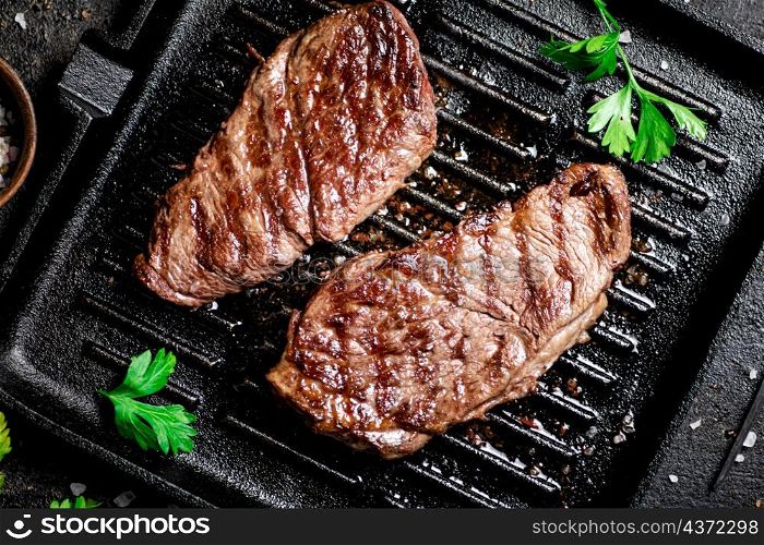 Grilled steak with parsley in a frying pan. On a black background. High quality photo. Grilled steak with parsley in a frying pan.