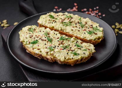 Grilled toast with avocado paste, eggs, cream cheese, salt, spices and herbs on a textured concrete table