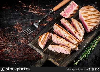 Grilled tuna on a cutting board. Against a dark background. High quality photo. Grilled tuna on a cutting board.