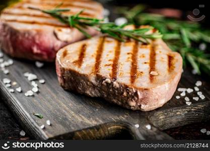 Grilled tuna on a cutting board with a sprig of rosemary. Against a dark background. High quality photo. Grilled tuna on a cutting board with a sprig of rosemary.