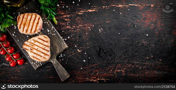 Grilled tuna on a cutting board with parsley and tomatoes. Against a dark background. High quality photo. Grilled tuna on a cutting board with parsley and tomatoes.