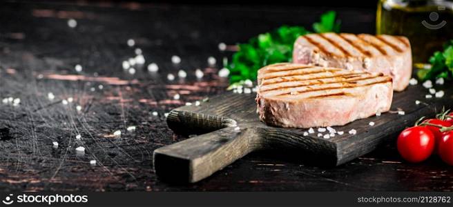 Grilled tuna on a cutting board with parsley and tomatoes. Against a dark background. High quality photo. Grilled tuna on a cutting board with parsley and tomatoes.