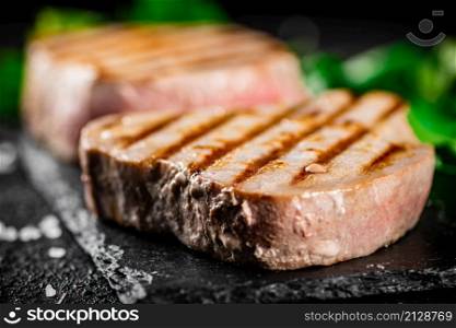 Grilled tuna on a stone board with parsley and salt. On a black background. High quality photo. Grilled tuna on a stone board with parsley and salt.
