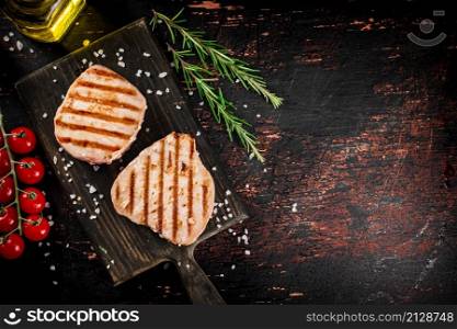 Grilled tuna steak on a cutting board with spices, cherry tomatoes and rosemary. Against a dark background. High quality photo. Grilled tuna steak on a cutting board with spices,cherry tomatoes and rosemary.