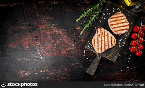 Grilled tuna steak on a cutting board with spices, tomatoes and rosemary. Against a dark background. High quality photo. Grilled tuna steak on a cutting board with spices, tomatoes and rosemary.