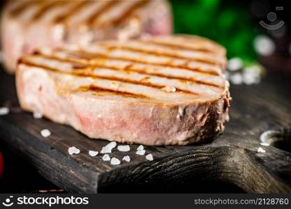 Grilled tuna steak on a parsley cutting board. On a black background. High quality photo. Grilled tuna steak on a parsley cutting board.