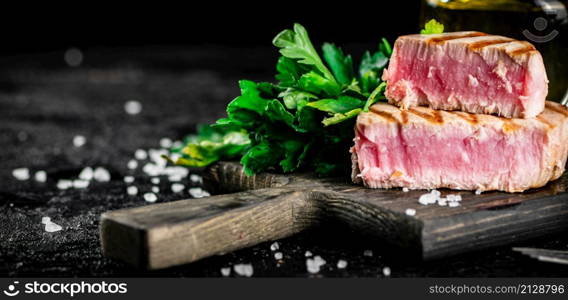 Grilled tuna steak on a parsley cutting board. On a black background. High quality photo. Grilled tuna steak on a parsley cutting board.