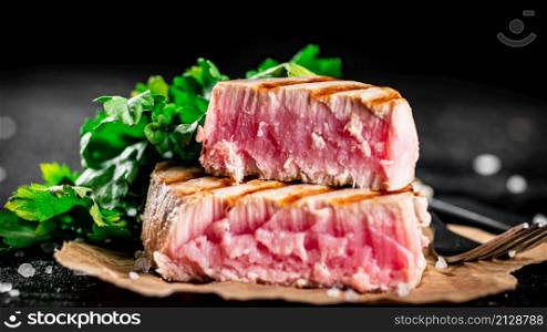 Grilled tuna with parsley on the table. On a black background. High quality photo. Grilled tuna with parsley on the table.
