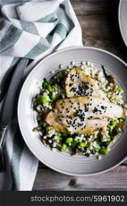 Grilled white fish fillet with mushroom risotto and edamame on rustic background