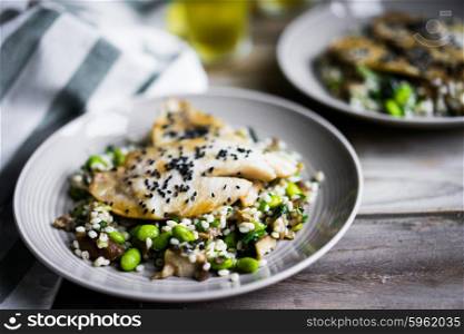 Grilled white fish fillet with mushroom risotto and edamame on rustic background