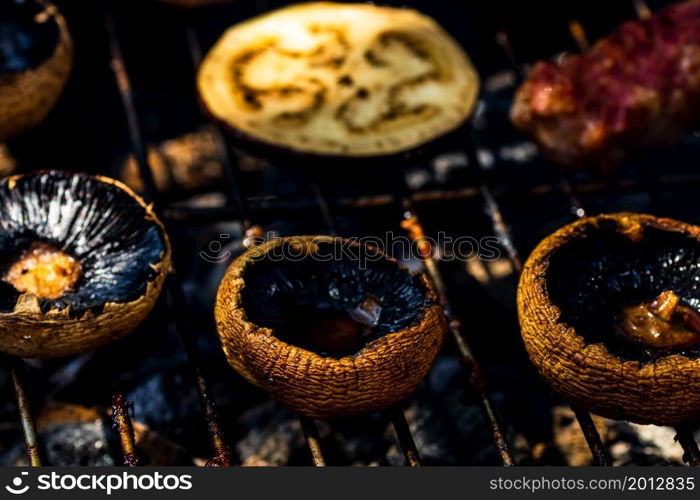 Grilling meat rolls called mici or mititei with vegetables on char barbecue. Charcoal grill with burning fire