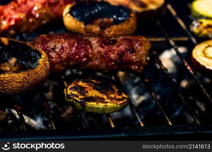 Grilling meat rolls called mici or mititei with vegetables on char barbecue. Charcoal grill with burning fire