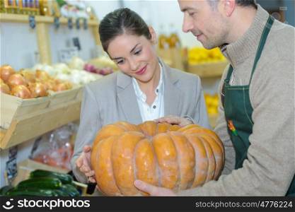 Grocer showing pumpkin to customer