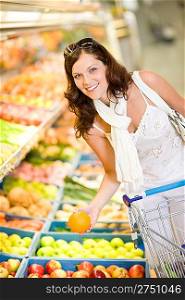Grocery store - smiling woman shopping with trolley in supermarket, holding orange