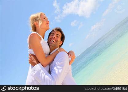 Groom and bride laughing on a sandy beach