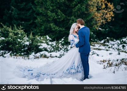groom in a blue suit and bride in white, embroidered with blue pattern, dress on a background of green pine forests in the mountains of the Carpathians