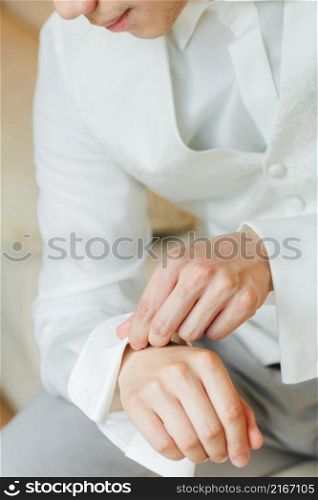 groom in a white tuxedo sitting pinning his shirt.. groom in a white tuxedo sitting pinning his shirt
