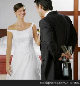 Groom looking at his bride and holding a bottle and glasses behind his back