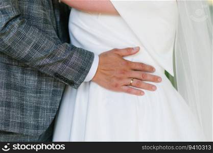 Groom&rsquo;s hand with the wedding ring lies on the bride&rsquo;s waist