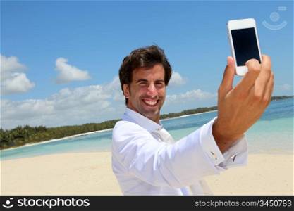 Groom taking picture of himself on a beach