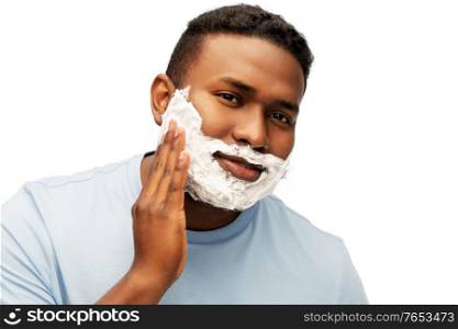 grooming and people concept - african american man applying shaving cream to his face over white background. african american man applying shaving foam to face