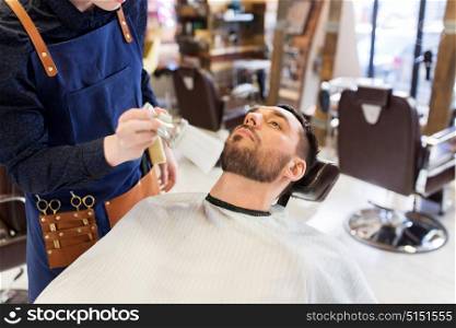 grooming and people concept - hairstylist cleaning client&rsquo;s face and beard with brush at barbershop. barber cleaning male face with brush at barbershop