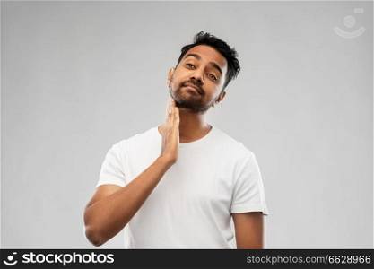 grooming and people concept - indian man touching his beard over gray background. indian man touching his beard