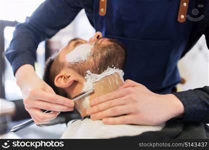 grooming and people concept - man and barber hands with straight razor shaving beard at barbershop. man and barber with straight razor shaving beard