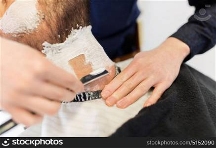 grooming and people concept - man and barber hands with straight razor shaving beard at barbershop. man and barber with straight razor shaving beard