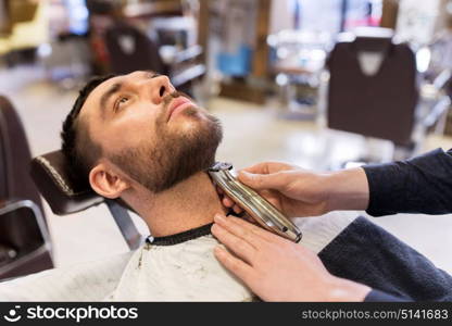 grooming and people concept - man and barber hands with trimmer or shaver cutting beard at barbershop. man and barber with trimmer cutting beard at salon