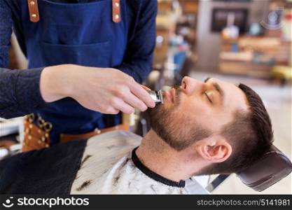 grooming and people concept - man and barber hands with trimmer or shaver cutting beard at barbershop. man and barber with trimmer cutting beard at salon