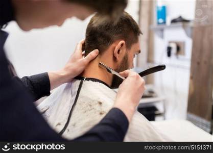 grooming and people concept - man and barber with straight razor shaving neck hair at barbershop. man and barber with straight razor shaving hair