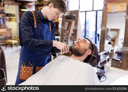 grooming and people concept - man and barber with trimmer or shaver cutting beard at barbershop. man and barber with trimmer cutting beard at salon
