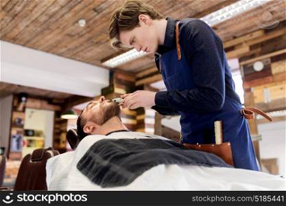 grooming and people concept - man and barber with trimmer or shaver cutting beard at barbershop. man and barber with trimmer cutting beard at salon