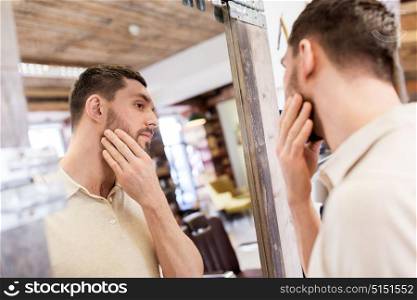 grooming and people concept - man looking at himself at barbershop mirror. man looking at himself at barbershop mirror