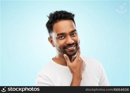 grooming and people concept - smiling indian man touching his beard over blue background. smiling indian man touching his beard